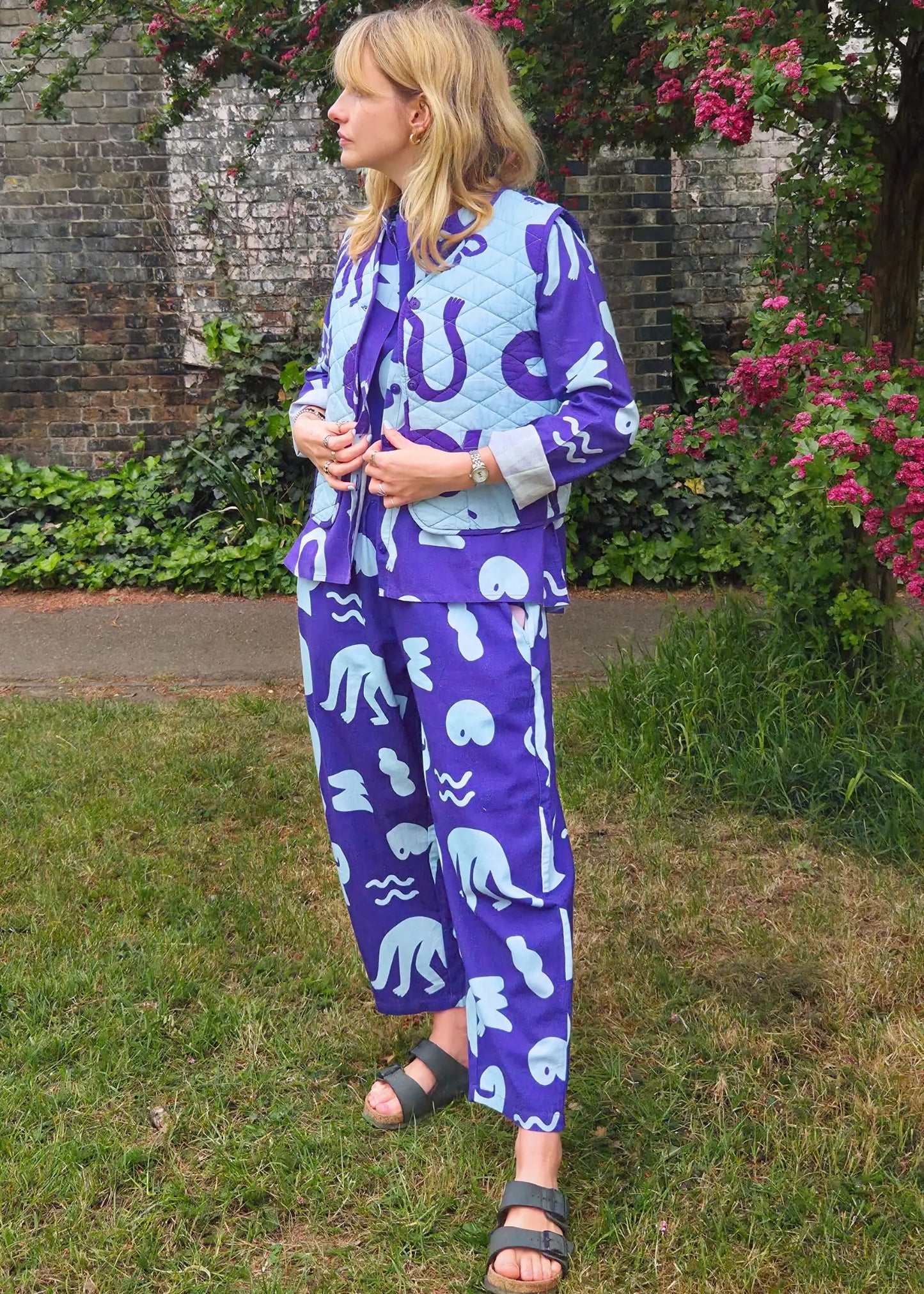 Woman wearing a blue and light blue patterned outfit standing in a garden.