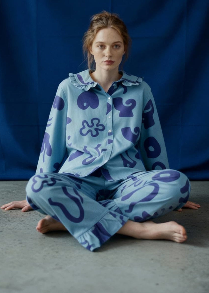 Person wearing a light blue pyjama set with dark blue patterns sitting on a grey floor against a blue curtain.