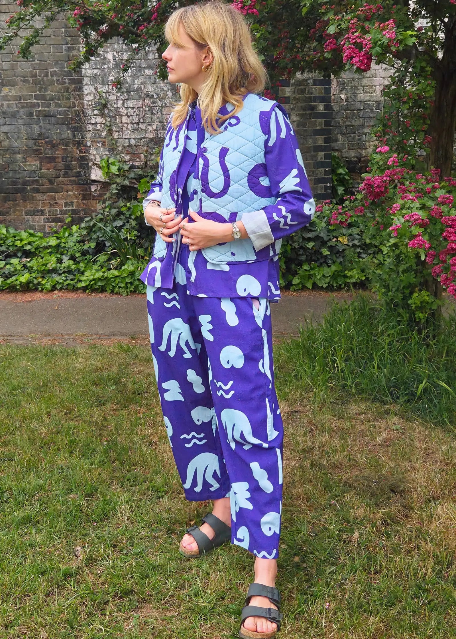 Woman wearing a blue and light blue patterned outfit standing in a garden.