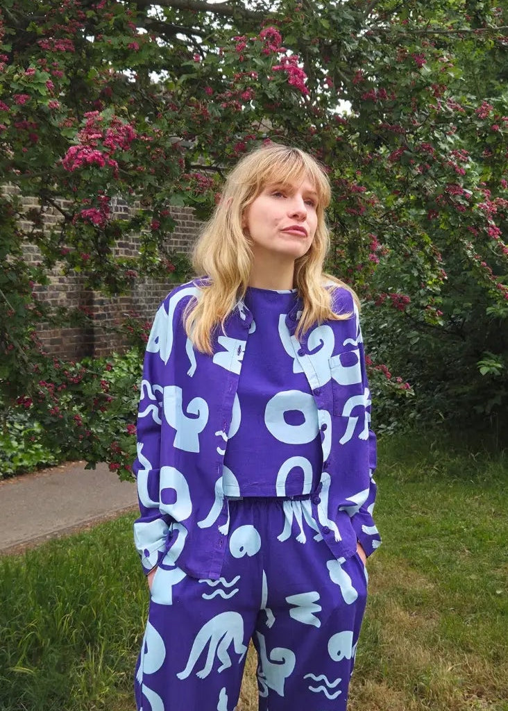 Person wearing a blue patterned outfit standing in a garden with trees and grass.