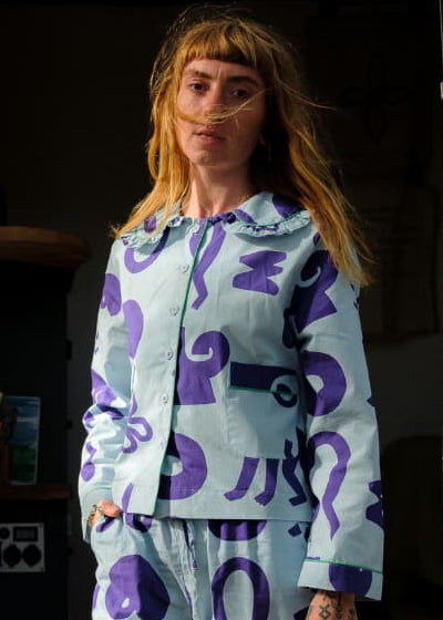 Woman in patterned pajamas standing in front of a camper van.