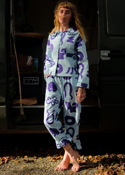 Woman in patterned pyjamas standing in front of a camper van.