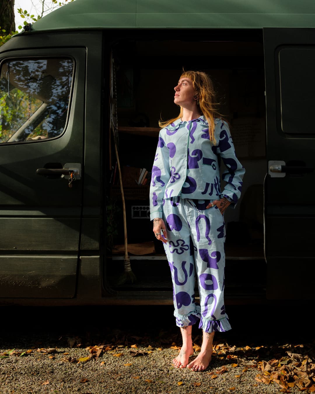 Woman in a patterned outfit standing in front of a camper van.