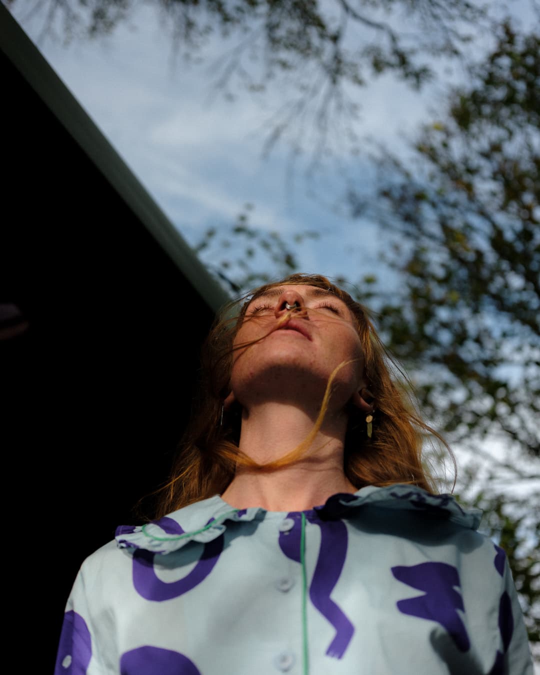 Person wearing a patterned jacket looking upwards with trees in the background