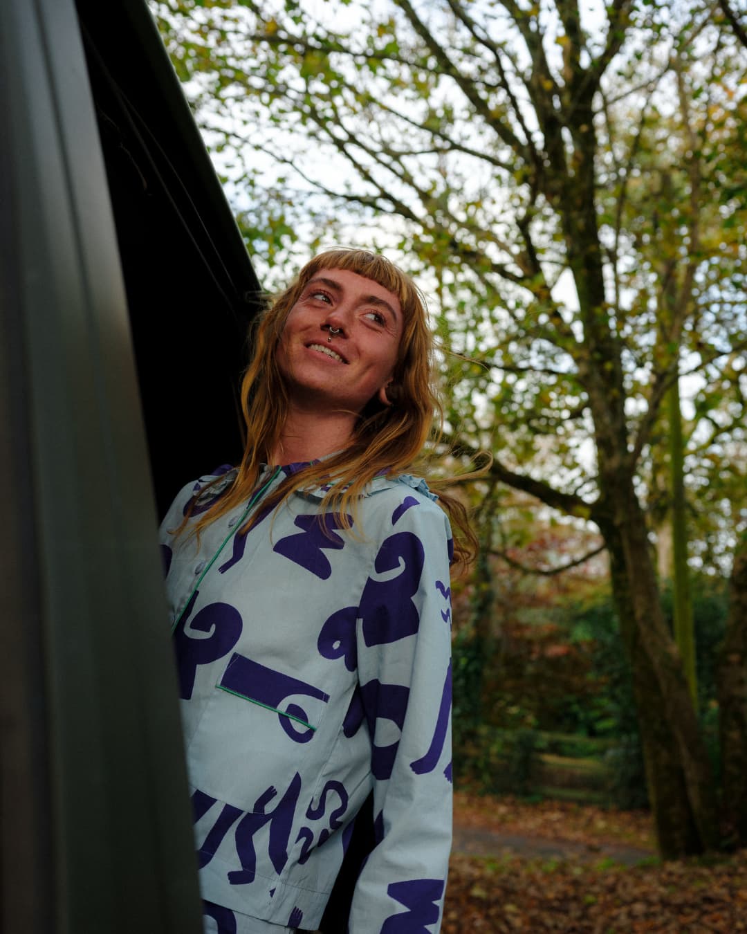 Person wearing a light blue hoodie with dark patterns standing outdoors with trees in the background