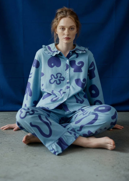 Person wearing a light blue pyjama set with dark blue patterns sitting on a grey floor against a blue curtain.