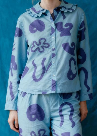 Woman wearing a light blue pajama set with purple patterns against a blue curtain.
