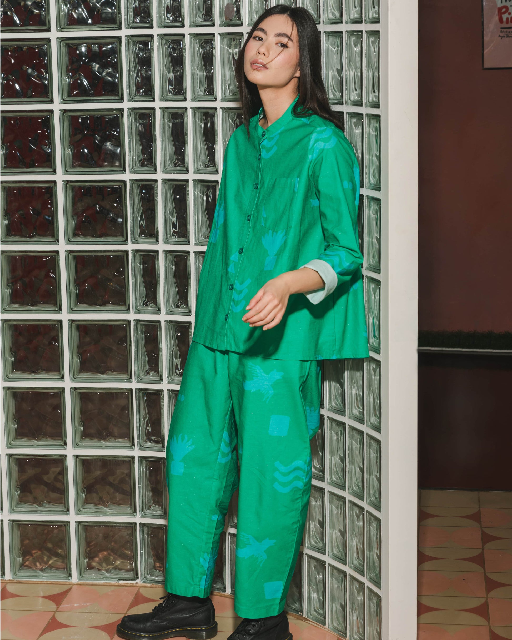 Person wearing a green outfit standing in front of a glass block wall.