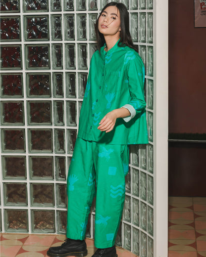 Person wearing a green outfit standing in front of a glass block wall.