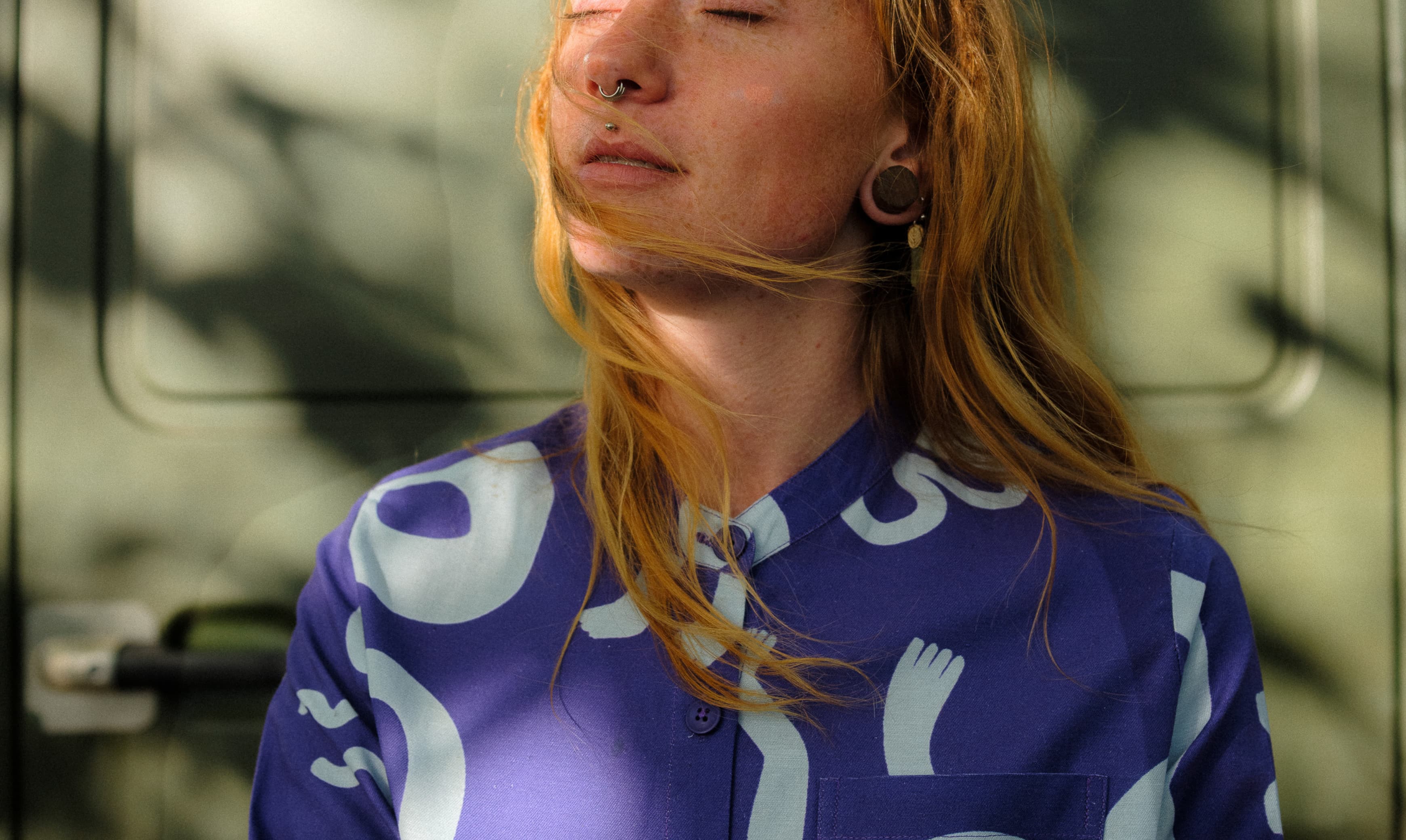 women closing eyes looking towards the sun in a blue patterned shirt