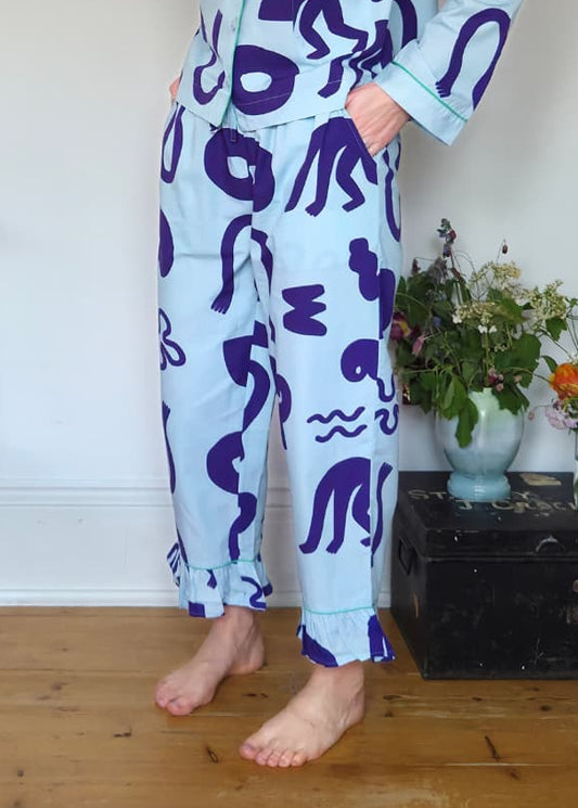 Woman wearing a light blue pyjama set with blue abstract patterns in a room with wooden floor and white walls.